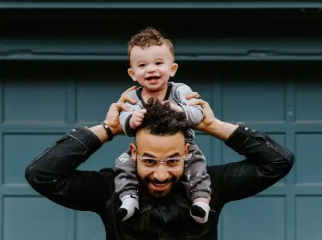 Ein Mann trägt ein Baby auf seinen Schultern und strahlt dabei Glück und Zufriedenheit aus. Dieser glückliche Moment zeigt, wie der Pluxee Benefit BGM PGB das Wohlbefinden von Mitarbeitenden fördert.