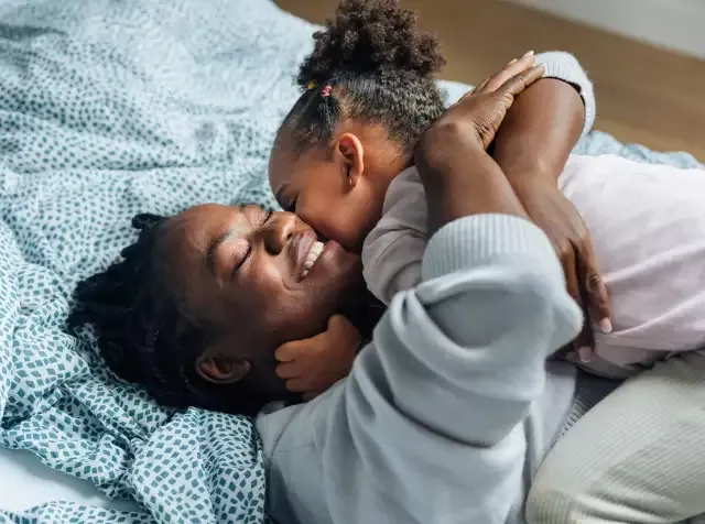 Eine Frau liegt gemeinsam mit ihrem Kind glücklich auf einem Bett und fühlt sich sicher, weil ihr Arbeitgeber ihr dank dem Pluxee Multibenefit Berufsunfähigkeit besten Versicherungsschutz bietet.