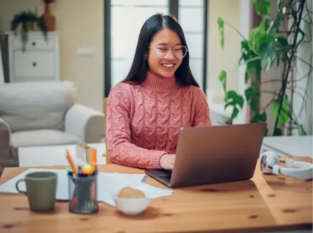 Eine Frau mit Brille sitzt an einem Tisch mit einem Laptop und arbeitet, während Ihr Arbeitgeber die Kosten für ihren privaten Internetanbieter übernimmt.