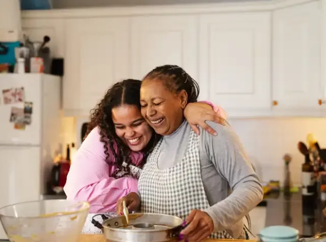Zwei glückliche Frauen in der Küche, die zusammen kochen und sich gegenseitig unterstützen.