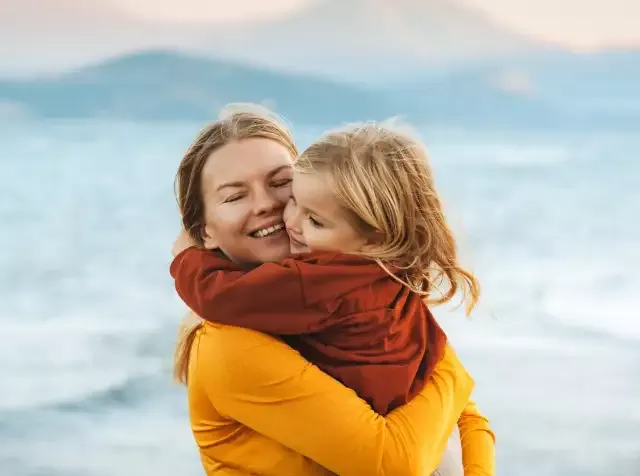 Eine Frau umarmt ihr Kind am Strand und genießt die gemeinsame Zeit, während sie von den Vorteilen des Betrieblichen Gesundheitsmanagements von Pluxee profitiert.